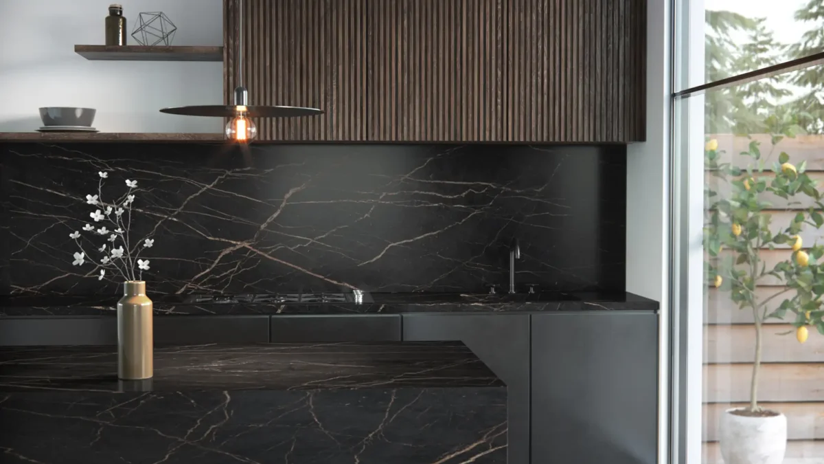 AKP DektonKitchen Laurent Moderne Küche mit dunklem Marmordesign. Eine Insel und Rückwand aus schwarzem Marmor mit goldenen Adern, darüber eine Hängelampe. Oberschränke aus Holz, daneben Pflanzen in Töpfen vor einer großen Glaswand.