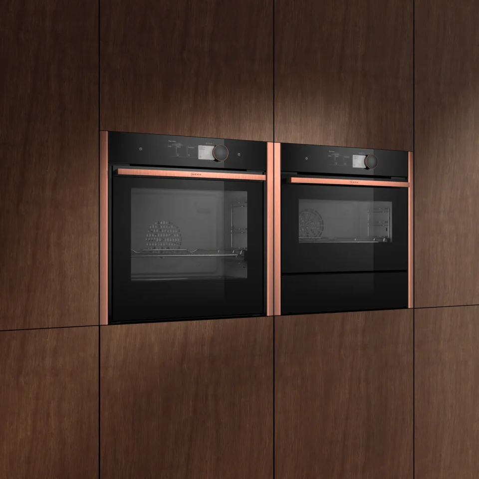 Einbaumöbel mit zwei nebeneinander liegenden, modernen Backöfen. Die Öfen haben schwarze Glastüren und Kupferakzente. Das Design wirkt elegant und minimalistisch.