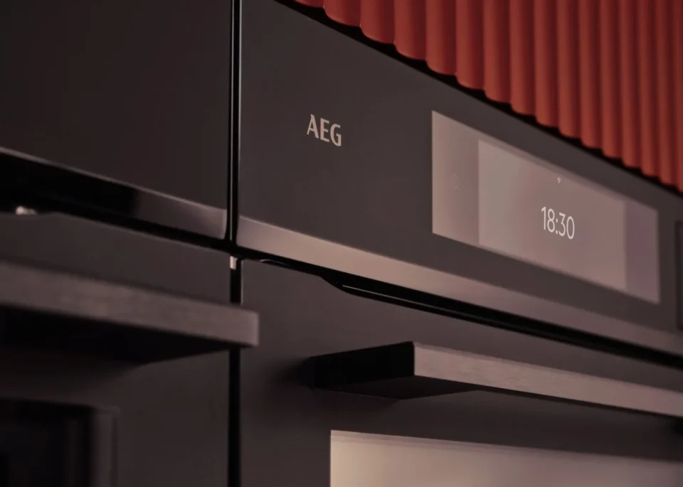 Nahaufnahme eines schwarzen AEG-Backofens mit digitaler Anzeige, die 18:30 Uhr anzeigt. Der Ofen hat eine glatte Oberfläche mit einem Griff und roten Akzenten im Hintergrund.