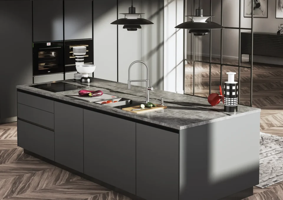 Moderne Küche mit einer großen, grauen Insel aus Stein. Auf der Arbeitsfläche liegen Gemüse und ein Schneidebrett. Hängelampen beleuchten den Raum. Im Hintergrund sind ein Ofen und Schränke zu sehen. Holzfußboden ergänzt das Design.