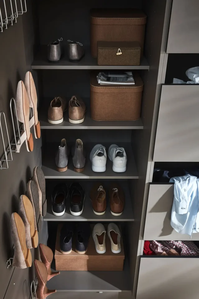 Ein Kleiderschrank mit mehreren Regalen zeigt eine geordnete Sammlung von Schuhen und Boxen. Links sind hohe Schuhe in Halterungen. Rechts sind Schubladen, von denen einige leicht geöffnet sind und Kleidung darin sichtbar ist.