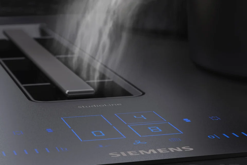 Eine Detailaufnahme eines Siemens Kochfelds mit integrierter Dunstabzugstechnologie. Auf dem glatten, dunklen Bedienfeld leuchten blaue digitale Anzeigen, während in der Mitte Dampf abgesaugt wird.