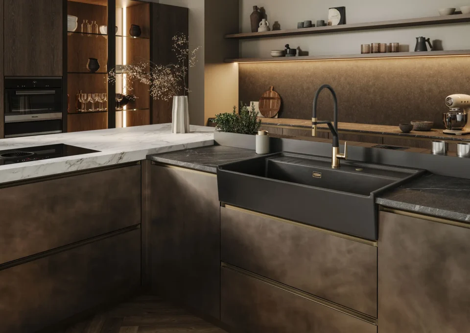 Eine moderne Küche mit matten, dunklen Schränken, einer großen schwarzen Spüle und einem goldenen Wasserhahn. Eine Kücheninsel mit Marmoroberfläche ist links. Im Hintergrund sind Regale mit Dekor und Geschirr.