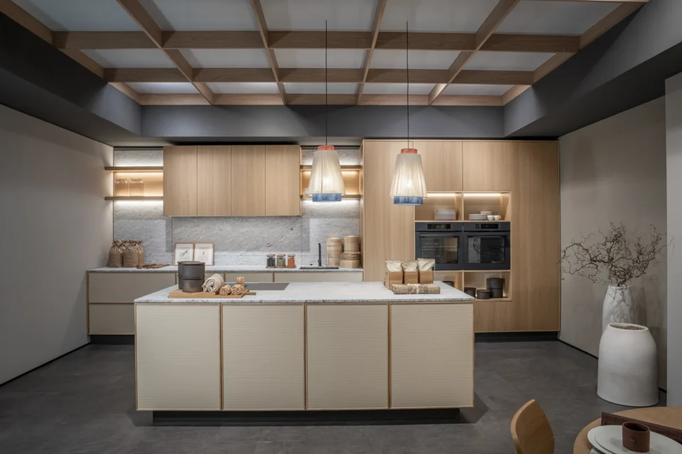 Moderne Küche mit Holzschränken, einer Kochinsel und drei hängenden Lampen. Grauer Boden, weiß-graue Arbeitsflächen, integrierte Geräte und dezent dekorierte Accessoires. Decke mit einem Gitter aus Holz und Akzentbeleuchtung.