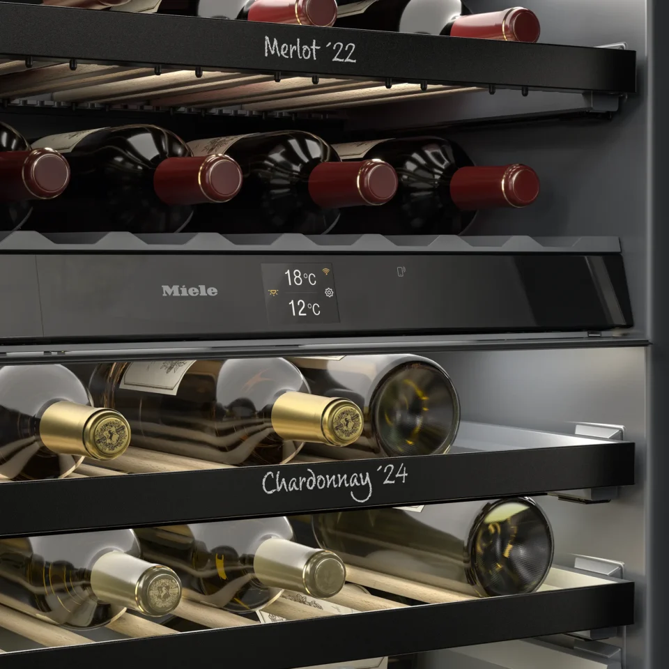 Weinkühlschrank mit mehreren Flaschen auf Regalen. Obere Reihe beschriftet mit "Merlot '22", untere mit "Chardonnay '24". Digitalanzeige zeigt Temperaturen von 18°C und 12°C.