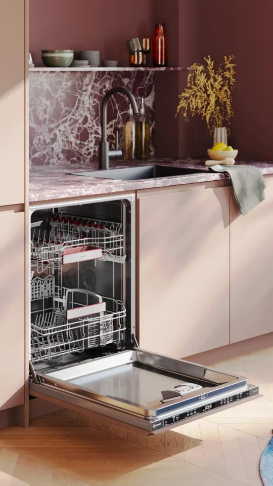 Ein moderner Geschirrspüler steht in einer stilvollen Küche offen. Die Küche hat eine Marmorplatte, ein Waschbecken und dekorative Objekte auf dem Regal. Der Geschirrspüler hat herausziehbare Körbe und edelstahlfarbene Innenflächen.