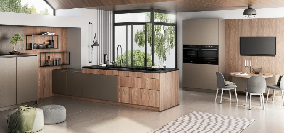 Moderne Küche mit Holz- und dunklen Schränken, einem Herd und Waschbecken. Draußen sind Bäume durch große Fenster sichtbar. Ein runder Tisch mit Stühlen steht rechts, Regale mit Dekor an der linken Wand.