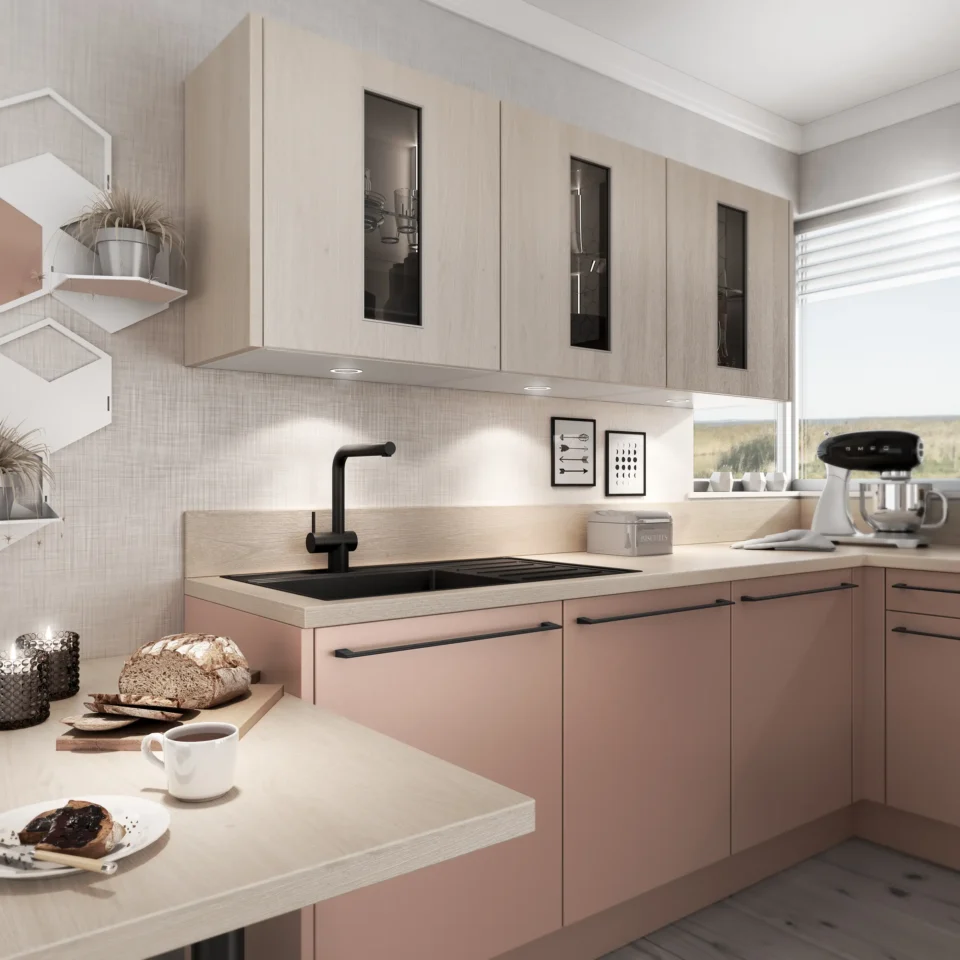 Helle und moderne Küche mit pastellrosa Unterschränken und hellen Hängeschränken. Auf der Arbeitsplatte stehen eine Brotmaschine und ein Teller mit Gebäck neben einer Tasse. Ein Fenster spendet natürliches Licht.