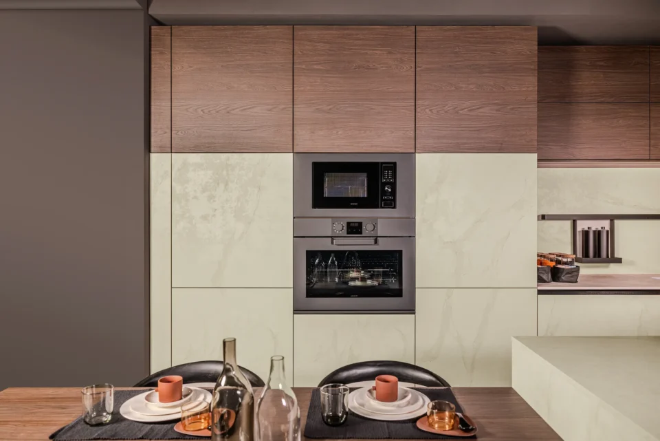Moderne Küche mit Holz- und hellen Schrankfronten. In der Mitte ein eingebauter Ofen und Mikrowelle. Im Vordergrund ein Tisch mit Platzdeckchen, Geschirr, Gläsern und Kerzen.
