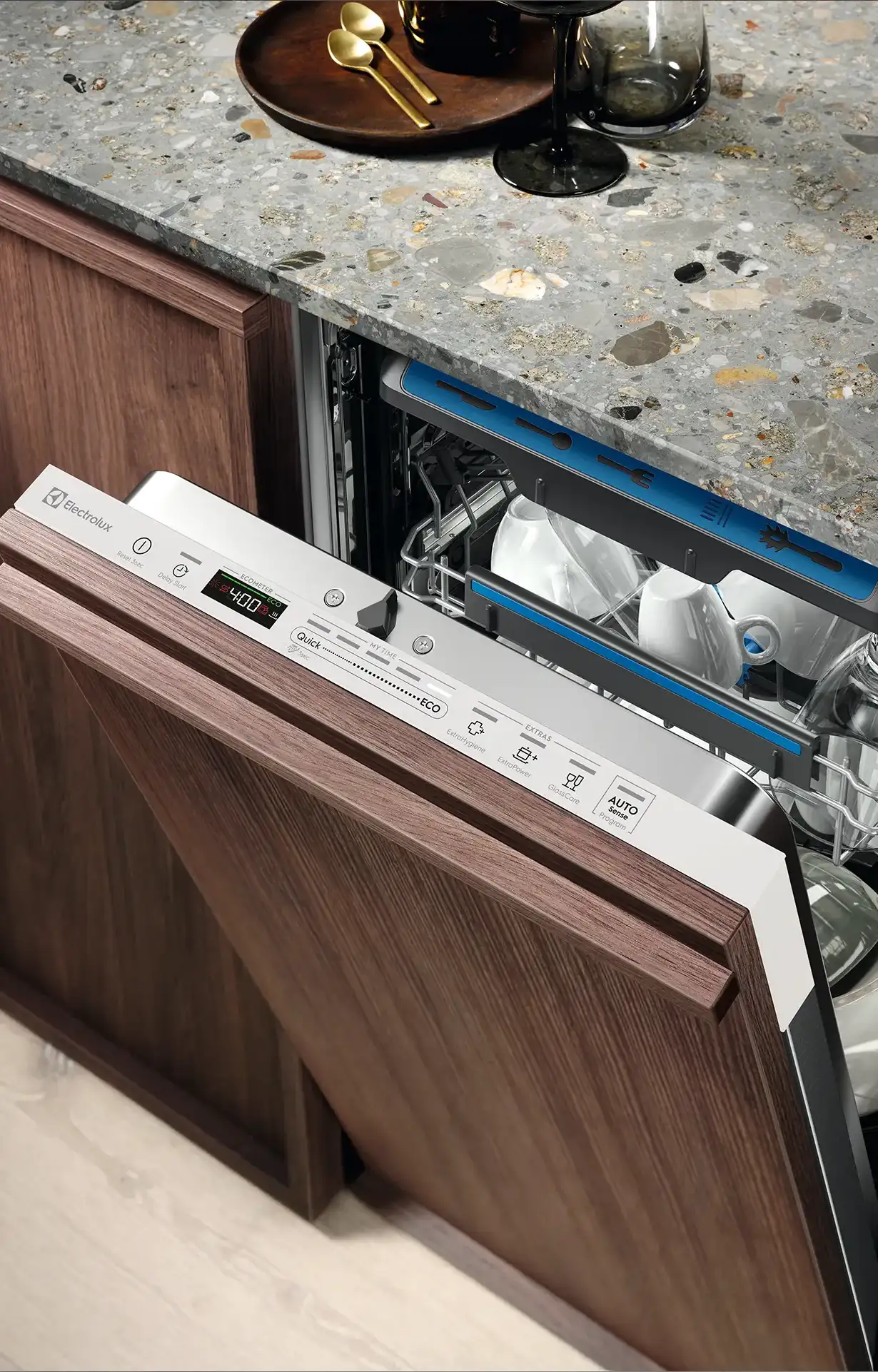 De Koeoek Marken List Electrolux Ein halb geöffneter Geschirrspüler in einer Küche ist zu sehen. Die Holzverkleidung passt zu den Küchenschränken. Oben befindet sich eine Steinplatte mit Tellern und Gläsern. Das Display zeigt verschiedene Waschoptionen.