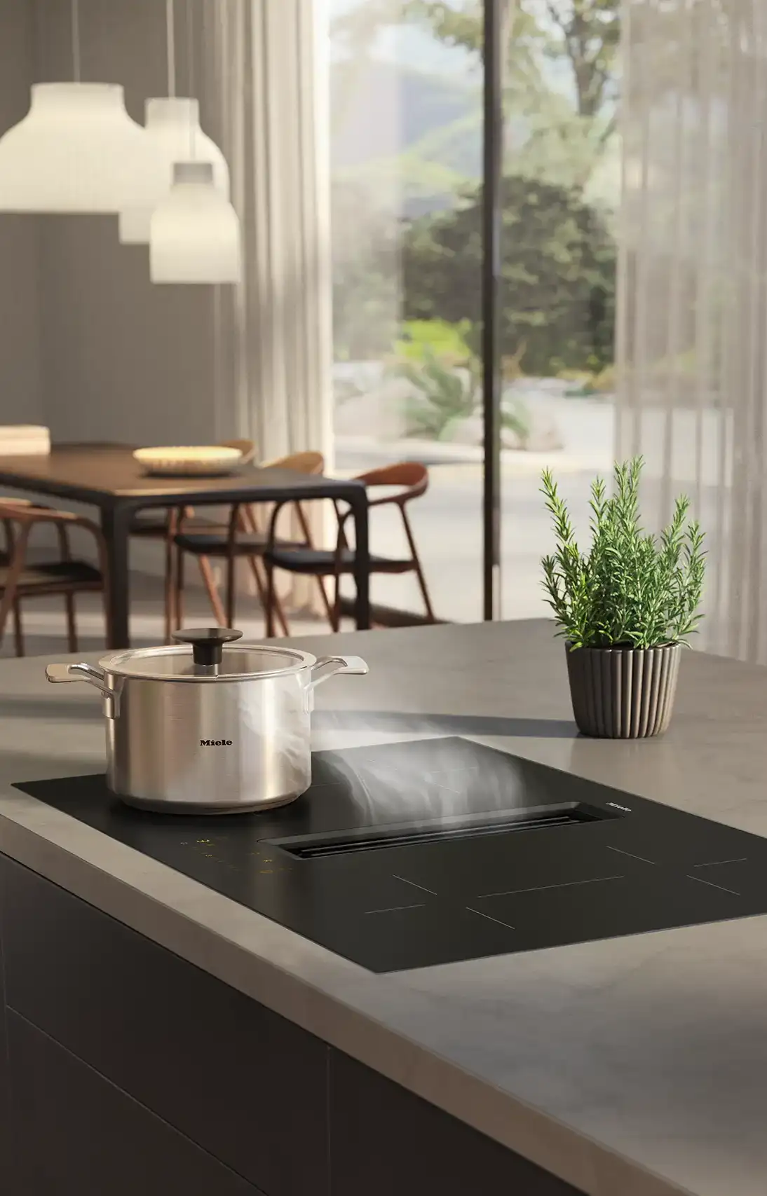De Koeoek Marken List Miele Eine moderne Küche mit einem Topf auf einem Induktionskochfeld. Im Hintergrund ist ein Esstisch mit Stühlen sichtbar, und durch große Fenster fällt Tageslicht herein. Eine Pflanze steht auf der Arbeitsfläche.