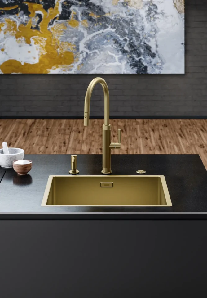 Ein stilvolles Küchendesign mit einem goldenen Wasserhahn und passendem Waschbecken in einer dunklen Arbeitsplatte. Im Hintergrund ein Marmormuster in Schwarz, Weiß und Gold auf der Wand. Der Boden ist aus Holz.
