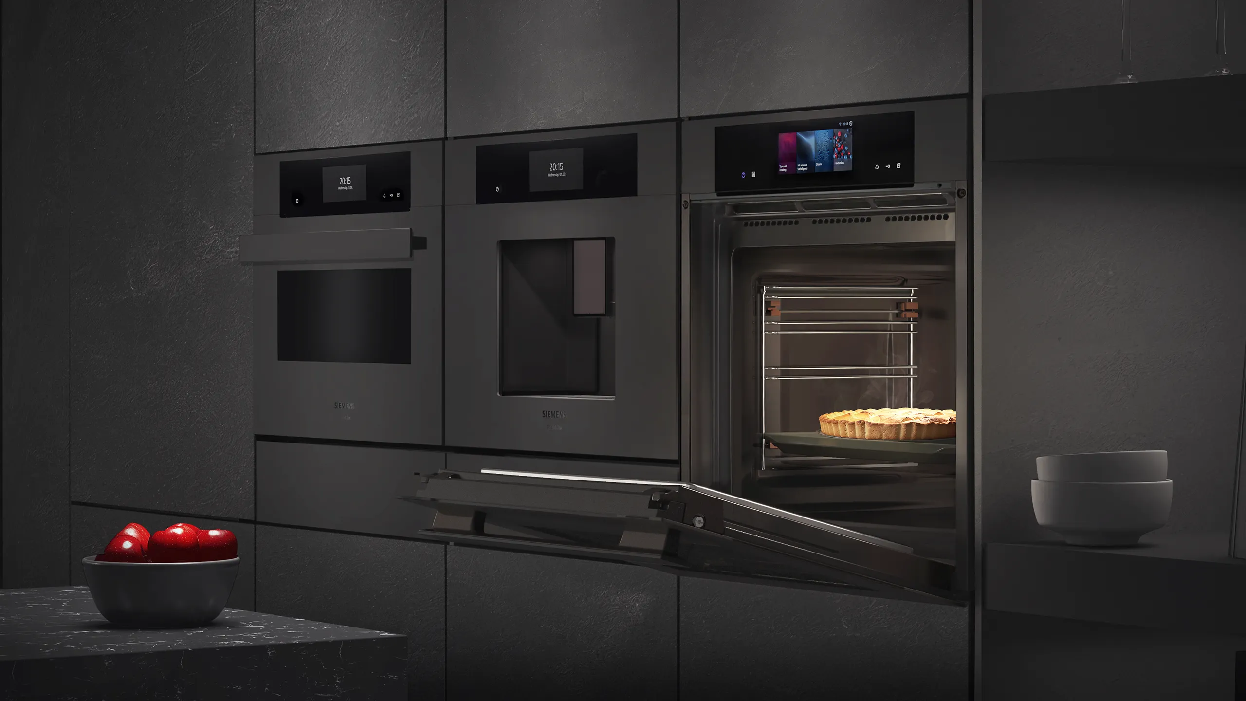 Eine moderne Küchenzeile mit grauen Schränken. Rechts ist ein geöffneter Einbau-Backofen zu sehen, in dem ein Kuchen auf einem Rost liegt. Links daneben sind zwei weitere geschlossene Geräte in die Schränke integriert.